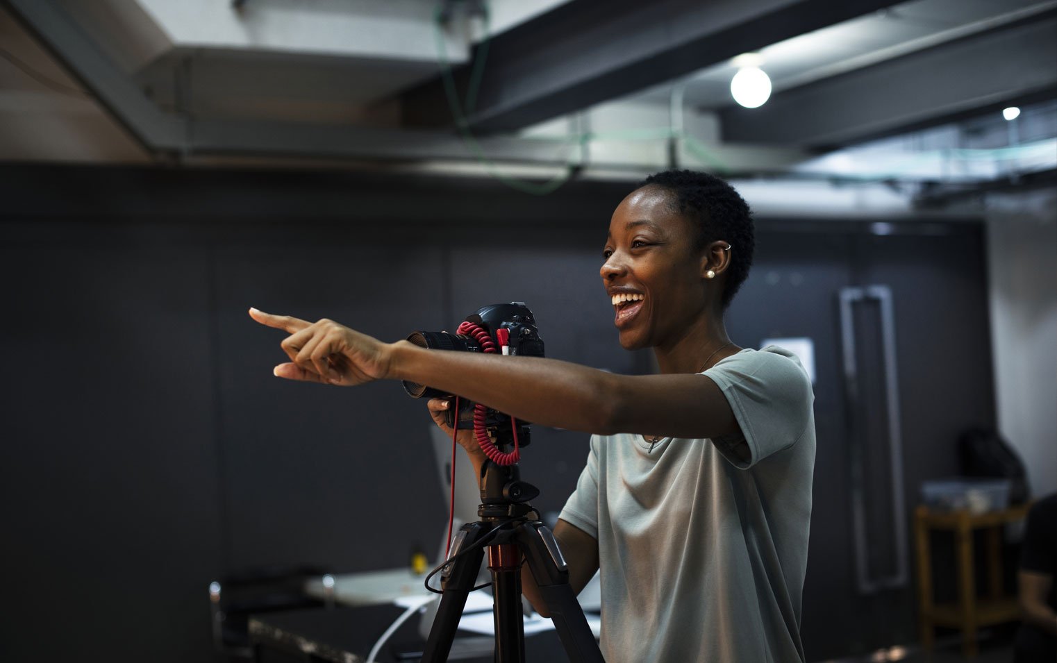 Smiling young African-American stands behind a camera on a tripod.